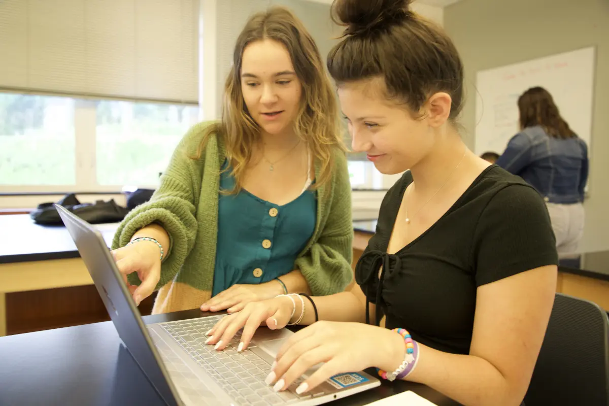 Woman points to girl's computer in classroom